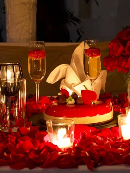 The complete romantic package: a beautiful cake, champagne on ice, and a table adorned with roses, all glowing in the soft light of candles.