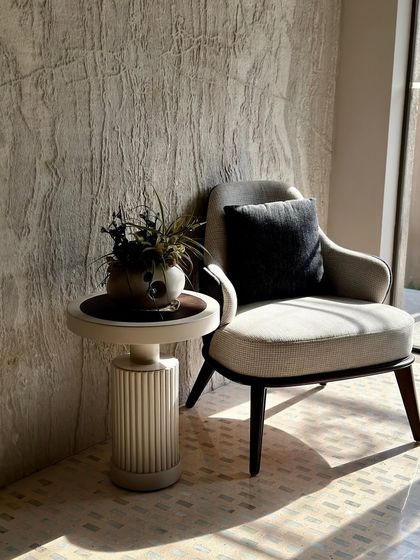 A closer view of the cozy corner, showing the interplay of light and shadow on the textured wall and the elegant forms of the furniture.