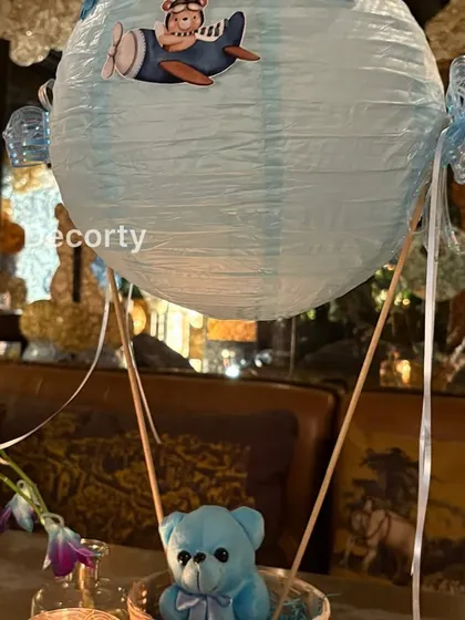 A detailed shot of the hot air balloon centerpiece, showing the delicate ribbons and the cute teddy bear passenger.