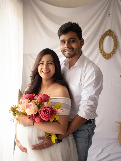 A bright and happy couple's maternity portrait. The fresh flowers and white backdrop create a clean, modern feel for this pregnancy announcement.