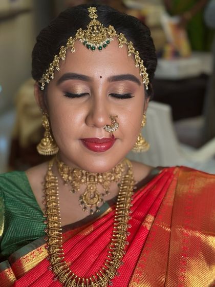 A close-up of Dr. Indhu's Muhurtham makeup with her eyes closed. This highlights the soft gold shimmer on her lids and the classic red lip, a perfect combination for a traditional bride.