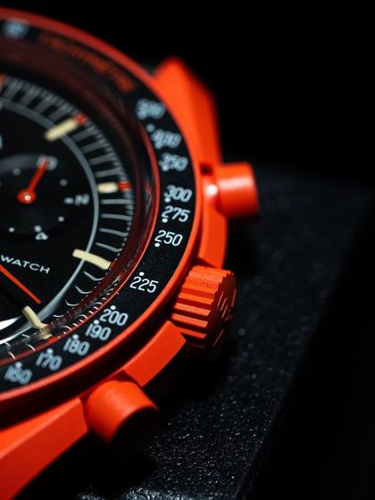 A detailed shot of the "Lava" Moonswatch, highlighting the contrast between the black dial and the bright orange case and chronograph pushers.
