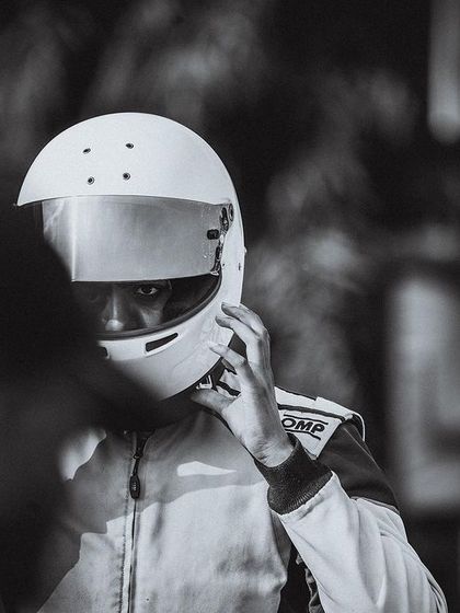 A black and white portrait of a driver adjusting his helmet, a timeless image of a racer preparing for battle.