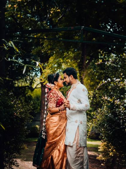 An intimate portrait of a South Indian couple, about to share a kiss amidst lush greenery, capturing the romance of their wedding day.