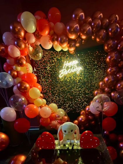 This wide shot captures the entire birthday setup, including the heart-shaped balloon arch, sequin wall, and romantic props like the 'LOVE' sign and light-up hearts on the table.