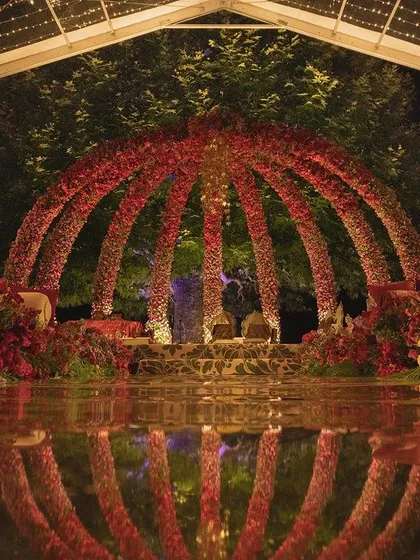 Under a clear tent, this magnificent dome-shaped mandap, covered in rich red florals, created a dramatic and intimate setting for a night wedding. The reflection on the mirrored aisle doubled the enchantment.
