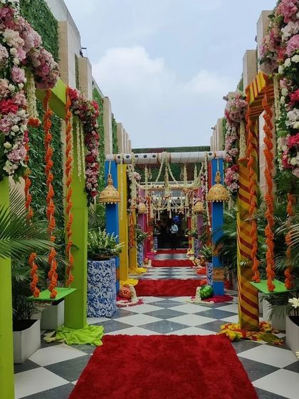 A wide view of the vibrant walkway for a Teej event, showing multiple decorated swings and colorful pillars that guide guests into the main celebration area.