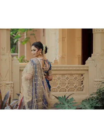 A classic bridal portrait. The bride looks over her shoulder with a gentle smile, her golden sheer dupatta catching the light beautifully against the ornate architectural background.