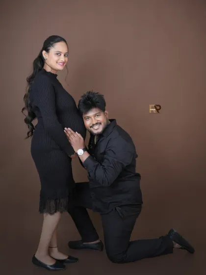 A playful and loving pose against a simple brown backdrop. The husband-to-be kneels to listen to the baby bump, capturing a sweet and classic maternity moment.