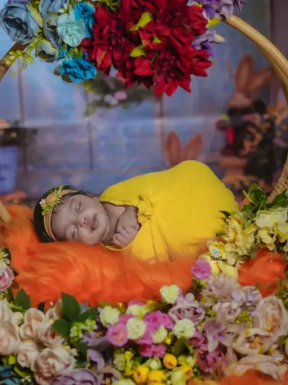A beautiful floral swing setup for a newborn girl. The vibrant colors of the flowers contrast beautifully with the baby's peaceful sleep, creating a stunning portrait.