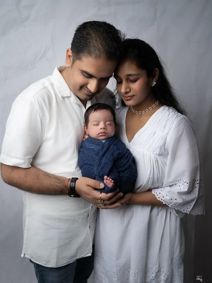 A tender moment captured in the studio. The parents' loving gaze and gentle hold create a timeless image of family love.