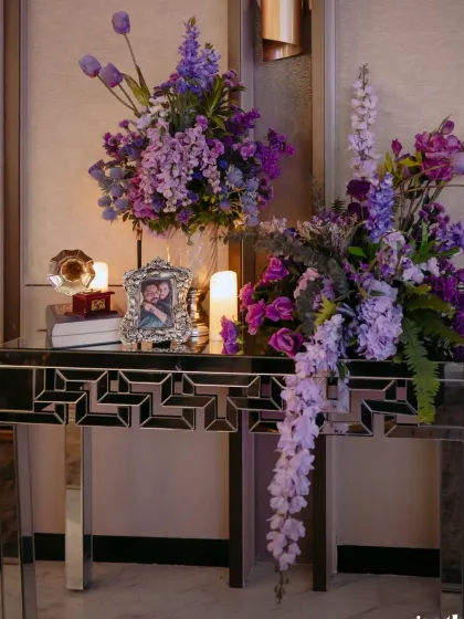 A corner of a welcome party, with lush purple floral arrangements and personalized photo frames, creating a space that is both beautiful and intimate.