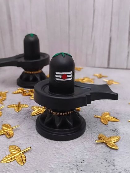 A pair of black Shiv Lingam idols, perfect for observing rituals like Maha Shivaratri. The golden leaves are for archana.