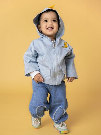 A joyful toddler in a blue hooded jacket and jeans walks with a big smile. His happy expression and cute outfit make for a heartwarming baby portrait.