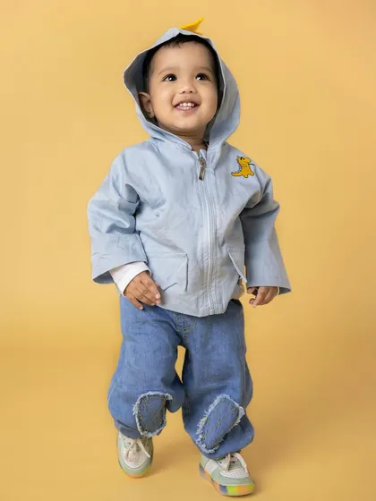 A joyful toddler in a blue hooded jacket and jeans walks with a big smile. His happy expression and cute outfit make for a heartwarming baby portrait.