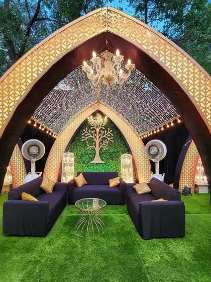 A stunning view of a bohemian Sangeet lounge area. The grand arch is decorated with gold lattice work and a chandelier, creating a luxurious yet relaxed seating space.