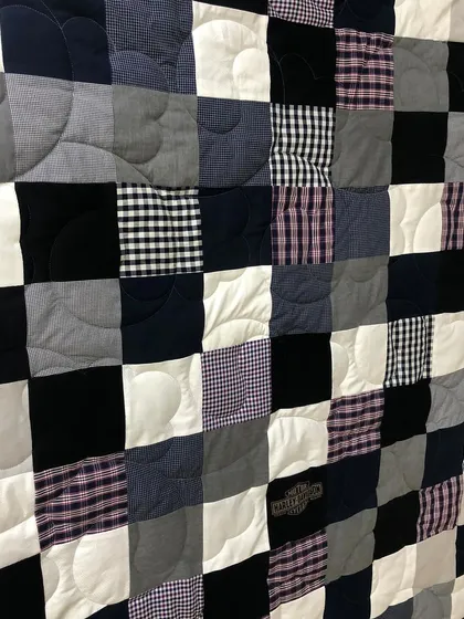 A memory quilt created from a collection of men's shirts and t-shirts, arranged in a classic patchwork design.