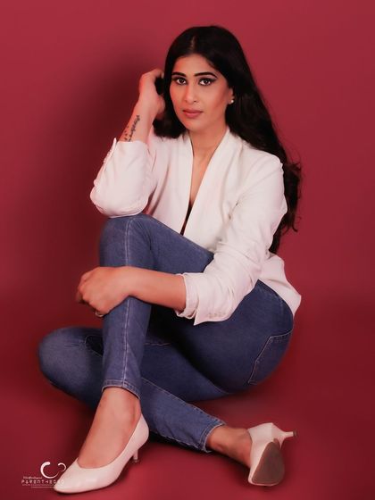 A relaxed, seated portrait that combines casual denim with a chic white blazer. The red background adds a pop of energy and confidence.