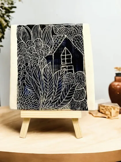 This decorative ceramic tile showcases the sgraffito technique, where I meticulously scratch through a layer of color to reveal the clay beneath. It's a piece of art that can be displayed on an easel or used as a unique tabletop accent.