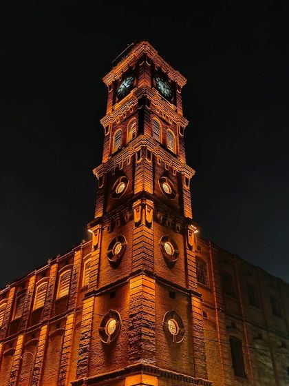 The clock tower of the Lal Imli Mill, standing tall against the night sky. A detailed architectural shot of a city landmark.