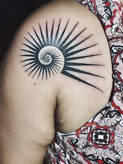 A geometric spiral sun tattoo on the shoulder.