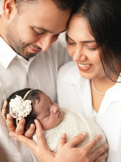 A new family of three, heads close together, admiring their newborn. The high-key lighting creates a soft, ethereal glow around them.