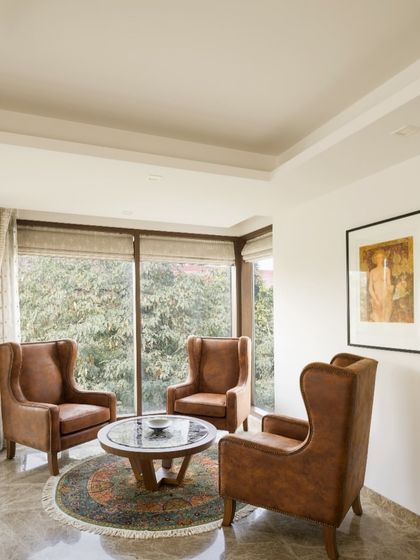 A cozy lounge corner at our Casa K project, featuring three high-back wing chairs in tan leather. We designed this nook by the French windows to be a quiet retreat for unhurried conversations and moments of stillness, framed by lush greenery.