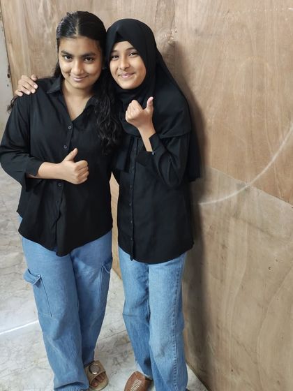 Two friends twinning in black shirts and blue jeans, giving a thumbs-up for the camera.