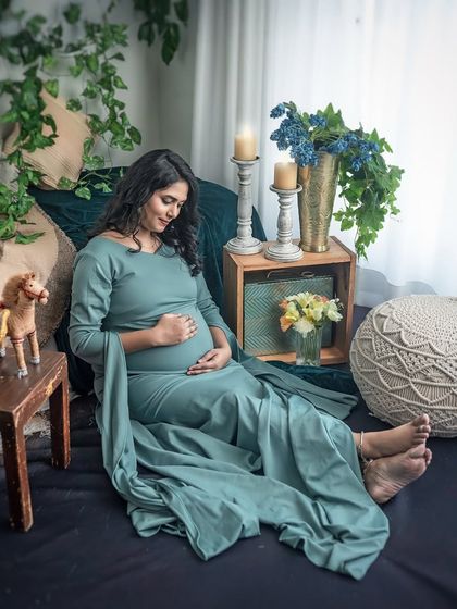 A relaxed and comfortable portrait in a beautiful sage green gown. The earthy tones of the bohemian setup, complete with wooden toys and woven cushions, create a cozy and inviting atmosphere.