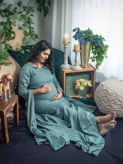 A relaxed and comfortable portrait in a beautiful sage green gown. The earthy tones of the bohemian setup, complete with wooden toys and woven cushions, create a cozy and inviting atmosphere.