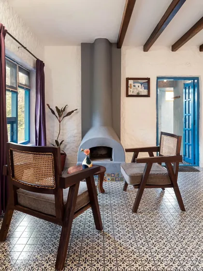 A cozy seating area by a fireplace in a Santorini-inspired villa. The blue-painted door and patterned floor tiles add a touch of Mediterranean color and flair to the rustic space.