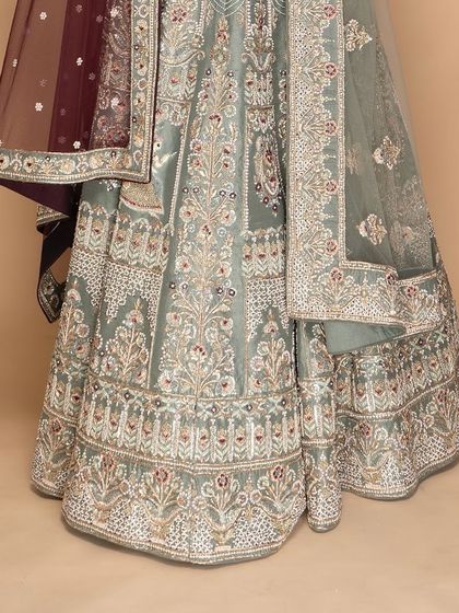 The skirt of this custom lehenga is a canvas of artistry. The delicate floral embroidery in muted tones on a sage green base creates a look of sophisticated, timeless elegance for any formal occasion.