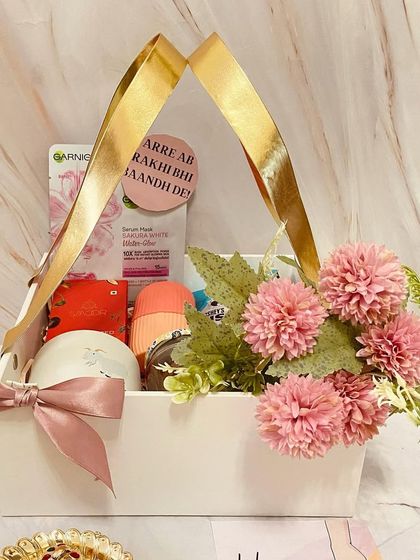 A pretty pink and white basket hamper for your sister. This gift includes a face mask and other pampering goodies, along with a funny tag that says 'Arre ab Rakhi bhi baandh de!'