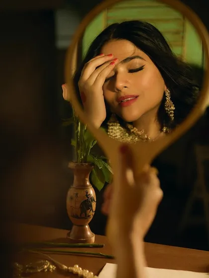 A creative shot using a hand mirror to frame Sakshi's face. This highlights the delicate eye makeup and the overall softness of the retro-inspired look.