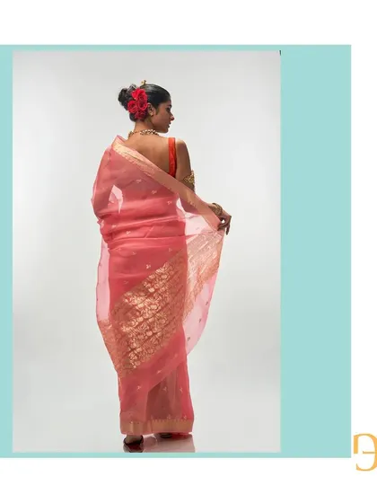 The back view of the salmon organza saree highlights the rich, floral gold zari work on the pallu, contrasting beautifully with the delicate buttis on the body.