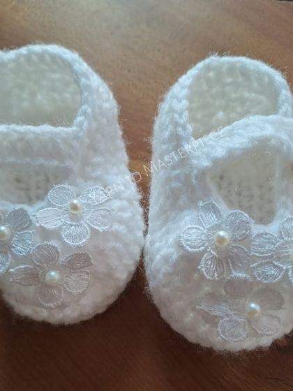 These white Mary Jane-style booties are perfect for a baptism. They are adorned with delicate lace flowers, each centered with a tiny pearl for a classic look.
