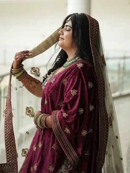 A candid shot of a bride in her velvet maroon lehenga. The open hair and minimal makeup create a look of simple, effortless elegance.