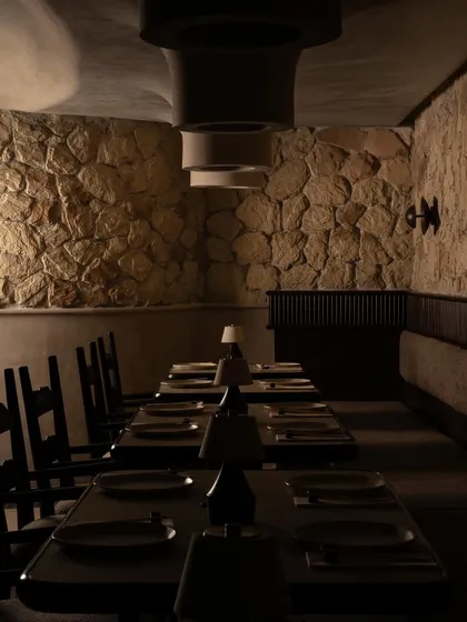 The private dining area at Call Me Ten, set against a backdrop of rough-hewn stone walls. The long communal table and minimalist chairs create a space that feels both ancient and modern, perfect for intimate gatherings.
