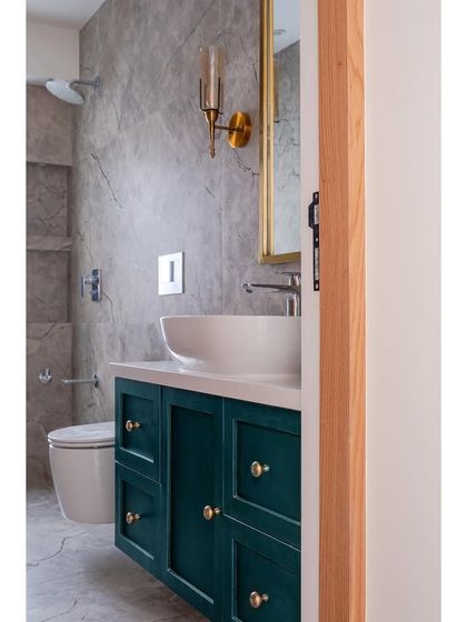 A single-colored tile runs through the walls and flooring of the parents' bathroom. A bottle green hued vanity with a gold mirror serves as the highlight of the area, adding a rich pop of color.