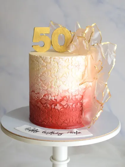 Turning 50 never looked so sweet! This cake features a beautiful red ombre effect with a delicate stencil pattern and is adorned with an elegant, edible rice paper sail.