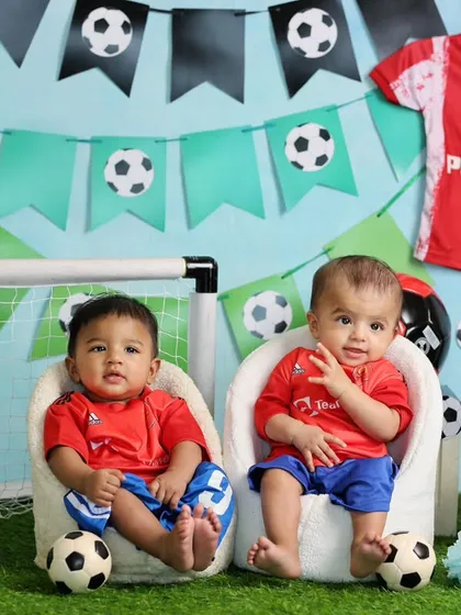 A football-themed half-birthday shoot for twins. Dressed in matching jerseys, they are surrounded by soccer balls and a mini goal post.