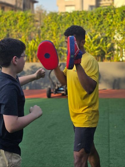 A young athlete practices his punches with a coach holding focus mitts. This interaction is key for learning proper form, timing, and distance management in a safe setting.