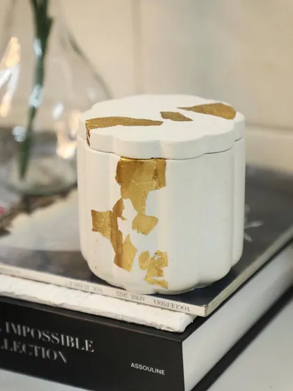 Our white Daisy Jar with gold leaf details, sitting elegantly on a stack of books. A perfect blend of modern and chic.