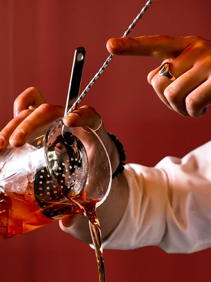 A close-up of a bartender's hands as they expertly pour from a mixing glass. This shot emphasizes the skill, focus, and steady hand required for perfect mixology.