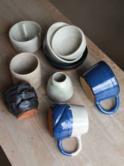 A stylish set of mugs and bowls in shades of blue, white, and black, some with altered forms and textured surfaces.