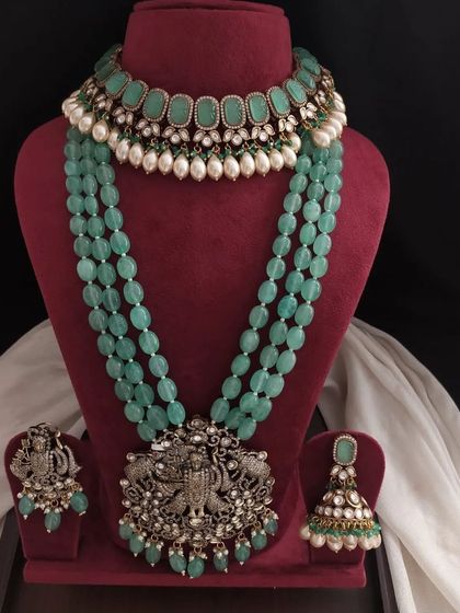 This pastel green set combines a choker with oval stones and a long beaded necklace with a deity pendant. The matching earrings complete this elegant ensemble.