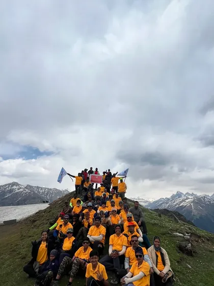 A group of trekkers at the summit of Chandrakhani Pass, with a panoramic view of the snow-capped peaks behind them.