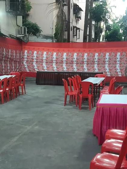 A simple and functional daytime setup for a small gathering. We arranged tables with pink skirting and red plastic chairs, providing a clean and practical space for guests to eat and sit.