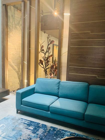 A bright teal sofa brings a pop of color to a neutral space, with the reflection of a sculptural tree visible in the background.