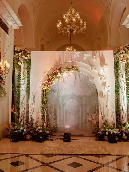 This grand entrance for a ring ceremony featured a floral-draped arch, classical statues, and a painted backdrop, creating a portal to an evening of timeless elegance.